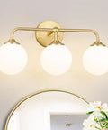 Dope Mid Century 3 Light Vanity Fixture With Smooth Brushed Gold Finish And Soft Milky White Glass Ball Shades mounted above a mirror.
