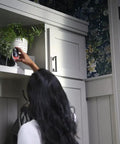 Person placing Cync Indoor Smart Camera With WiFi 1080p HD Night Vision on a shelf near plants for easy home surveillance.
