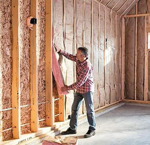 Person installing Two Pack R13 Pink Kraft Faced Fiberglass Insulation Rolls For 2x4 Wall Cavities 15 Inches By 32 Feet in a wall.