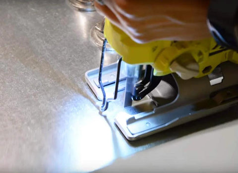 Close-up of a jigsaw with blade installed cutting metal on a workbench.