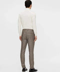 Rear view of a man wearing a white long-sleeve top and brown plaid trousers, standing against a plain background.