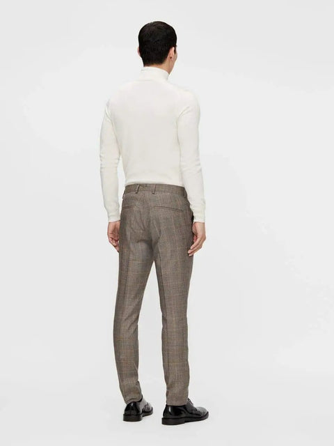 Rear view of a man wearing a white long-sleeve top and brown plaid trousers, standing against a plain background.