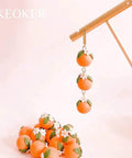 Handmade polymer clay orange bead earrings with floral accents hanging on display with a pile of matching beads below.