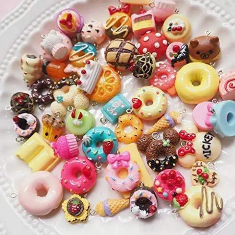 Assorted colorful miniature dessert charms on a plate, including donuts, ice cream cones, and cupcakes with decorative toppings.