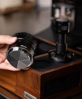 Universal 58mm Espresso Coffee Distributor With Gravity Tumbler For Standard Portafilters, held in hand over wooden base.