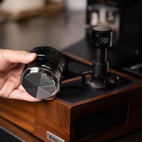 Universal 58mm Espresso Coffee Distributor With Gravity Tumbler For Standard Portafilters, held in hand over wooden base.