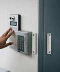 Person using keypad beside wired magnetic reed door contact sensor with two wires for normally closed NC applications on wall.