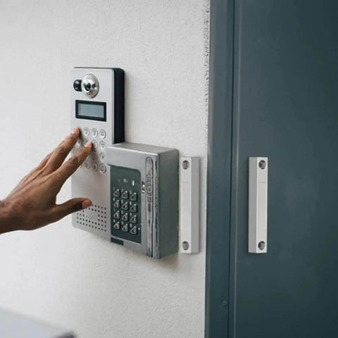 Person using keypad beside wired magnetic reed door contact sensor with two wires for normally closed NC applications on wall.