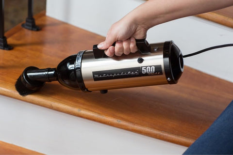 Person using Evolution Hand Vacuum Portable 120V 504W With All Steel Construction For Dry Pickup At Home Office Or Car Satin Nickel Black Ultra Powerful Yet Lightweight For Quick Cleanups Everywhere on wooden stairs
