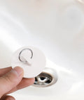 Heavy Duty Rubber Sink Stopper And Bathtub Drain Plugs Built Tough With A Slick Hang Loop, held above sink, white color, 2-inch size.
