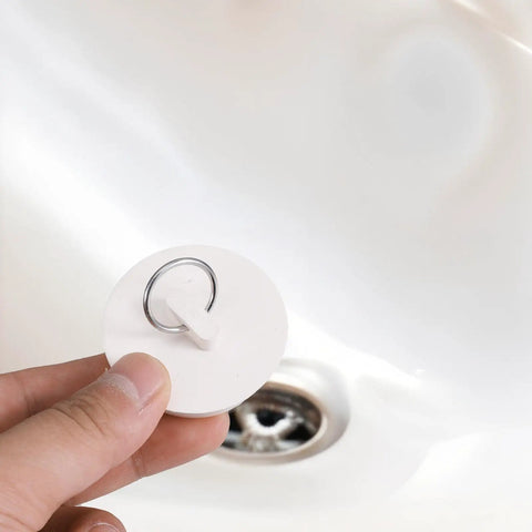Heavy Duty Rubber Sink Stopper And Bathtub Drain Plugs Built Tough With A Slick Hang Loop, held above sink, white color, 2-inch size.