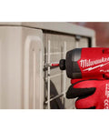 Milwaukee FUEL cordless drill with Shockwave bit, red body and black grip drilling into a gray metal cabinet.