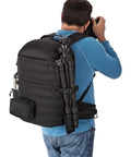 Person carrying an All Weather Camera Backpack With Padded 15.6 Inch Laptop Compartment, tripod attached, outdoor setting