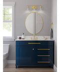 Bathroom with Adley Collection 3 Light Clear Glass Bath Vanity Light In Satin Brass over blue vanity, mirror reflection visible.