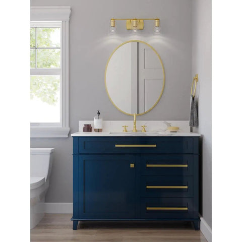 Bathroom with Adley Collection 3 Light Clear Glass Bath Vanity Light In Satin Brass over blue vanity, mirror reflection visible.