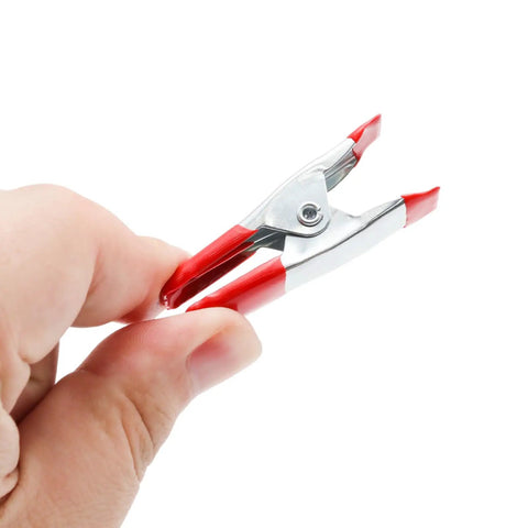 Close-up of a hand holding a 20 Pack 2 Inch Spring Clamps With Rubber Tips For Woodworking Camping Photography Furniture Crafts And Backdrops.