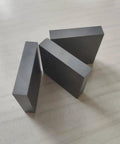 Three hardwearing boron carbide ceramic square sheets 10mm by 50mm by 50mm shown on a surface for scientific research insulating plate use.