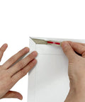 Hands sealing a 22 Pack White Rigid Mailers 9.25 X 11.5 Inches Heavy Duty Cardboard Mailer