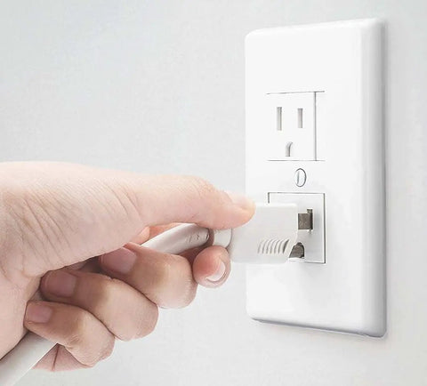 Hand unplugging a cord from a white self-closing outlet cover for center screw outlets, 3 inches wide by 4.75 inches high, 6 pack.
