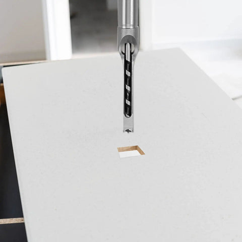 These Kickass Woodworking Drill Bits Feature Two Top Notch Square Hole Chisels For Fast Hollow Mortising On Any Lumber Project Including Half And Five Sixteenths Inch Sizes Today with drill bit in action creating square hole on white surface.