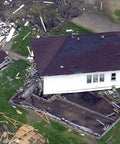 Aerial view of a house partially collapsed and damaged during a disaster, debris scattered around the surrounding area.