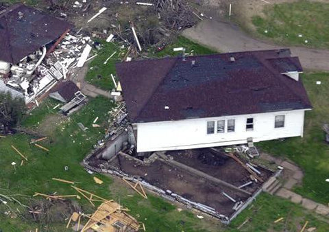 Aerial view of a house partially collapsed and damaged during a disaster, debris scattered around the surrounding area.