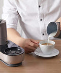 Mini Espresso Maker With Dual Pressure Extraction And Silky Milk Frother Styled Like A Classic Moka Pot One Touch Timer pouring frothed milk into a cup.
