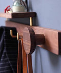Wall Mounted Coat Rack Featuring Dope Top Shelf For Keys And Jackets Solid Hardwood Construction Plus Durable Brass Hooks Hella Sturdy Design Effortless Entryway Makeover Totally Sleek Modern Finish close-up shows hooks and shelf with belts hanging.