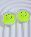 Four Pack Tiny Circular Bubble Levels With Double Sided Adhesive Backing Stick On Spirit Level Gauges For Quick Layouts And Precise Leveling On Cabinets Walls Tile And DIY Projects On The Go. 25mm neon acrylic circular levels on white surface