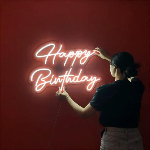Person adjusting Neon LED Birthday Sign USB Powered Acrylic Wall Light on red wall, glowing 'Happy Birthday' text, 16.3x10.2 inches