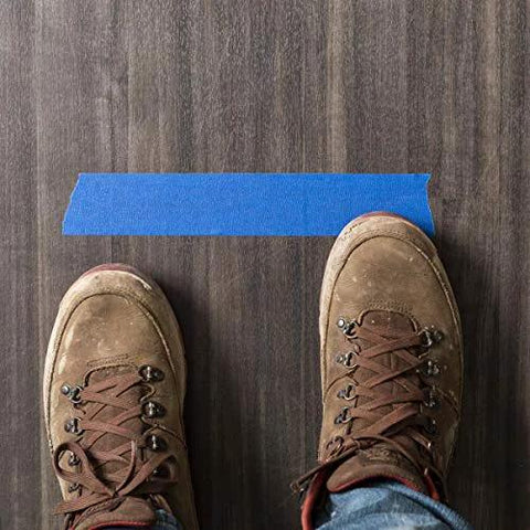 Blue painter's tape strip on dark wood floor, viewed from above with brown boots.