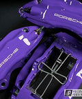 Purple Porsche brake calipers with white PORSCHE lettering and chrome hardware; Prismatic Powders watermark.