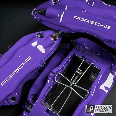 Purple Porsche brake calipers with white PORSCHE lettering and chrome hardware; Prismatic Powders watermark.