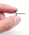 Close-up of Prime Bronze Flat Head Thumb Tack held in fingers, showcasing sturdy iron core and design for crafts and office use.
