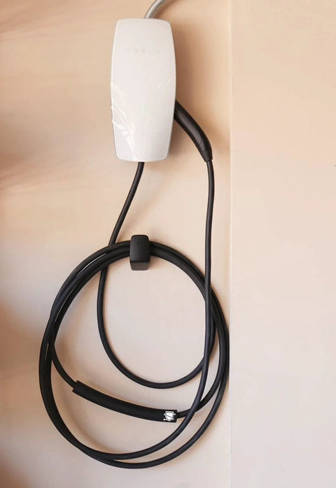 Front view of white Tesla EV cable protector mounted on wall with a coiled black charging cable for garage pass-through.