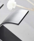 Close-up of waterfall spout deck mount bathroom faucet slick matte black finish with pop up drain no overflow modern lavatory.