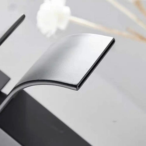 Close-up of waterfall spout deck mount bathroom faucet slick matte black finish with pop up drain no overflow modern lavatory.