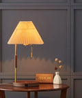 USB Wireless Charging Desk Lamp With Wood And Gold Finish on wooden table, featuring pleated shade and decor elements.