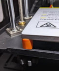 Close-up of Silicone Bed Mounts And Spacers Kit for 3D printers showing orange spacer on Ender 3 V2 heat bed for leveling.