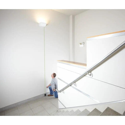 Person using Blaze Green Beam Laser Measure Up To 165 Feet With Real Time Distance Reading indoors to measure wall height.