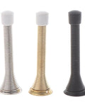 Three metal door stoppers with white rubber tips in silver, gold, and black finishes shown in a vertical standing position.
