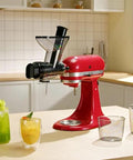 Front view: red KitchenAid stand mixer with black masticating juicer attachment.