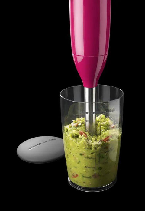 Hella Convenient 2 Speed Hand Blender With Slick Soft Grip Handle Built For Effortless Soups And Smoothies Featuring UltraLight 8 Inch Blending Arm And Roomy 3 Cup Bpa Free Jar In Bold Cranberry blending guacamole in a clear jar.