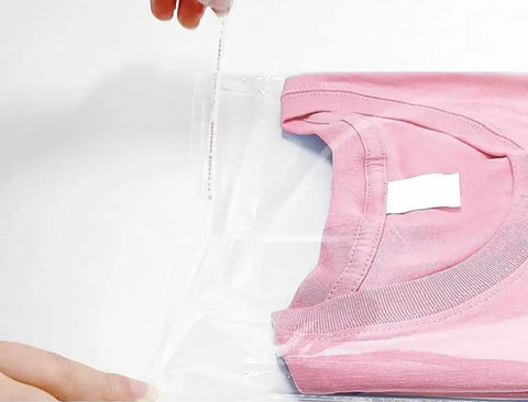Person sealing a pink t-shirt in a 100 Pack Clear 9x12 Inch Self Adhesive Plastic Bag For Packaging Clothes And T Shirts Peel And Seal.