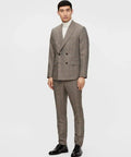 Man in a gray double-breasted checkered suit with white turtleneck and black shoes, standing against a white background