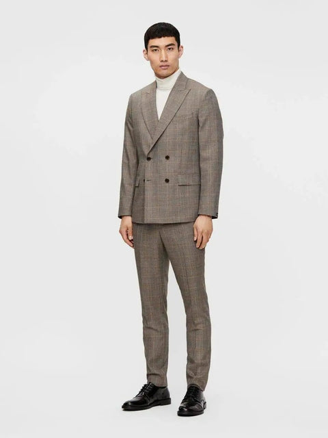 Man in a gray double-breasted checkered suit with white turtleneck and black shoes, standing against a white background