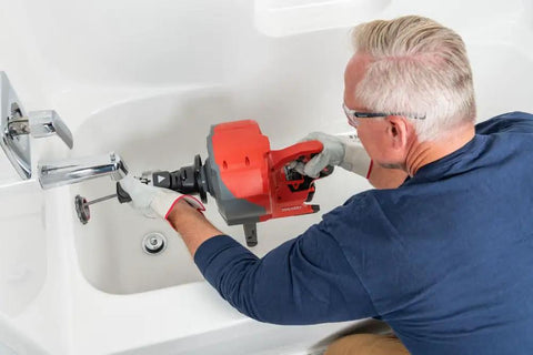 Person using Heavy Duty Cordless Drain Snake With Brushless Motor And Twenty Five Foot Steel Cable to clear a tub drain.