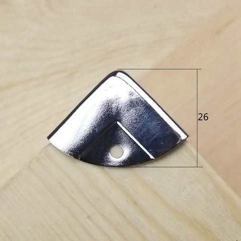 Close-up of a silver metal corner protector on wood, part of 12 Piece Decorative Corner Protectors for Cabinets and Furniture.