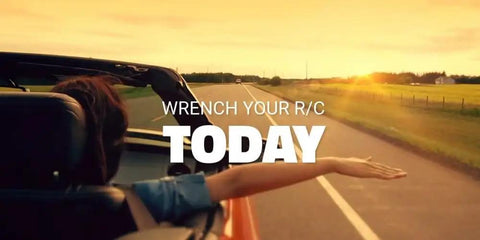 Person in a convertible car reaching out, text overlay reads 'Wrench Your R/C Today' with a sunset road view.