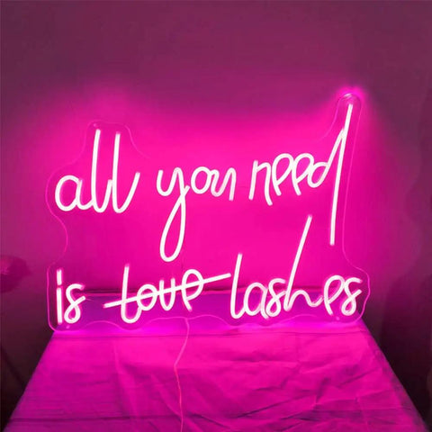 All You Need Is Lashes LED Neon Light Sign Pink 20 Inch for Wall Decor displaying luminous pink text on wall.